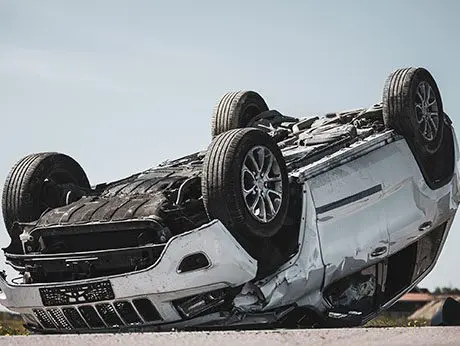 Horrific Traffic Accident, Rollover Smoking and Burning Vehicle Lying on its Roof in the Middle of the Road after Collision. Daytime Crash Scene with Severely Damaged Modern SUV Car.