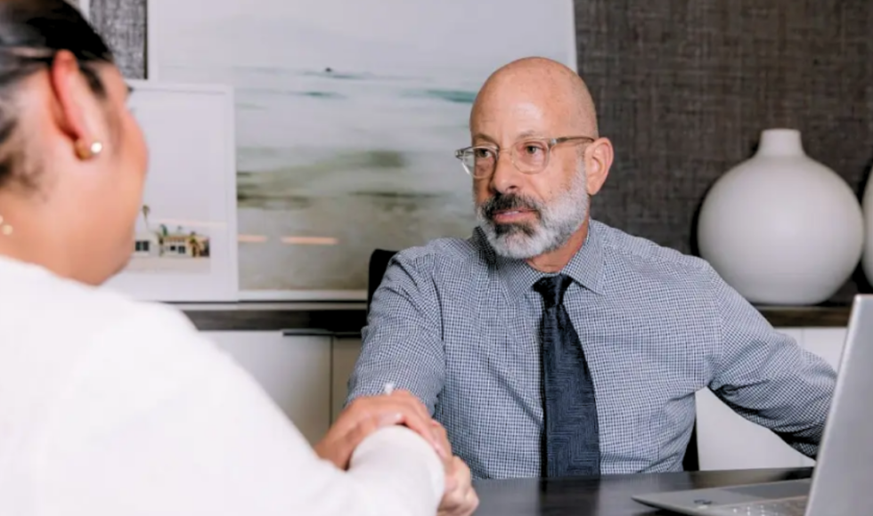 Personal injury attorney Eugene Bruno sitting at a desk in front of his laptop, shaking hands with a woman