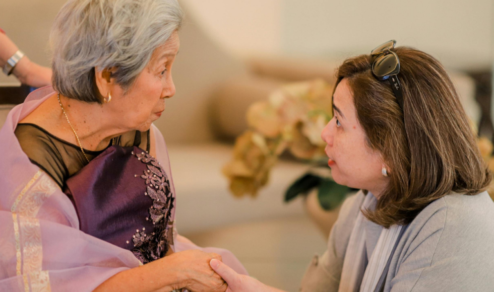 Adult daughter holding hands with elderly mother during a conversation at home, illustrating family discussions about aging parent safety, elder care planning, and emotional support for seniors.