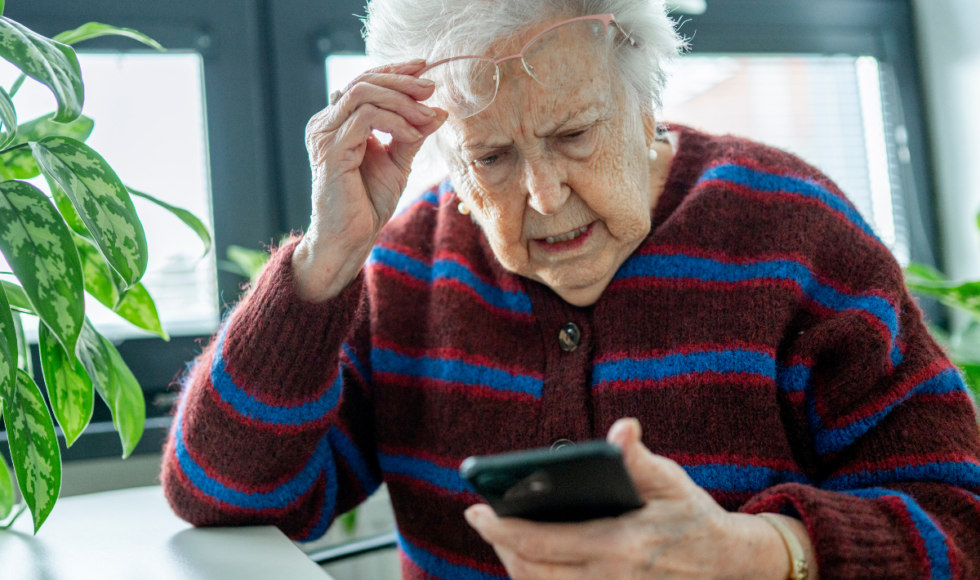 Elderly woman looking confused while using a smartphone, illustrating senior phone scam risks, financial exploitation concerns, and the importance of protecting older adults from fraud and identity theft.