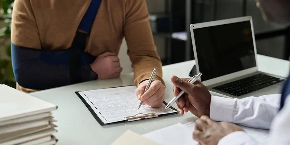 Injured man wearing an arm sling discussing paperwork with a medical professional